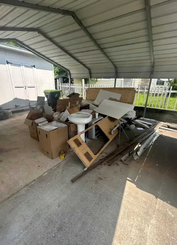 Mixed boxes, wood, and furniture under a covered driveway